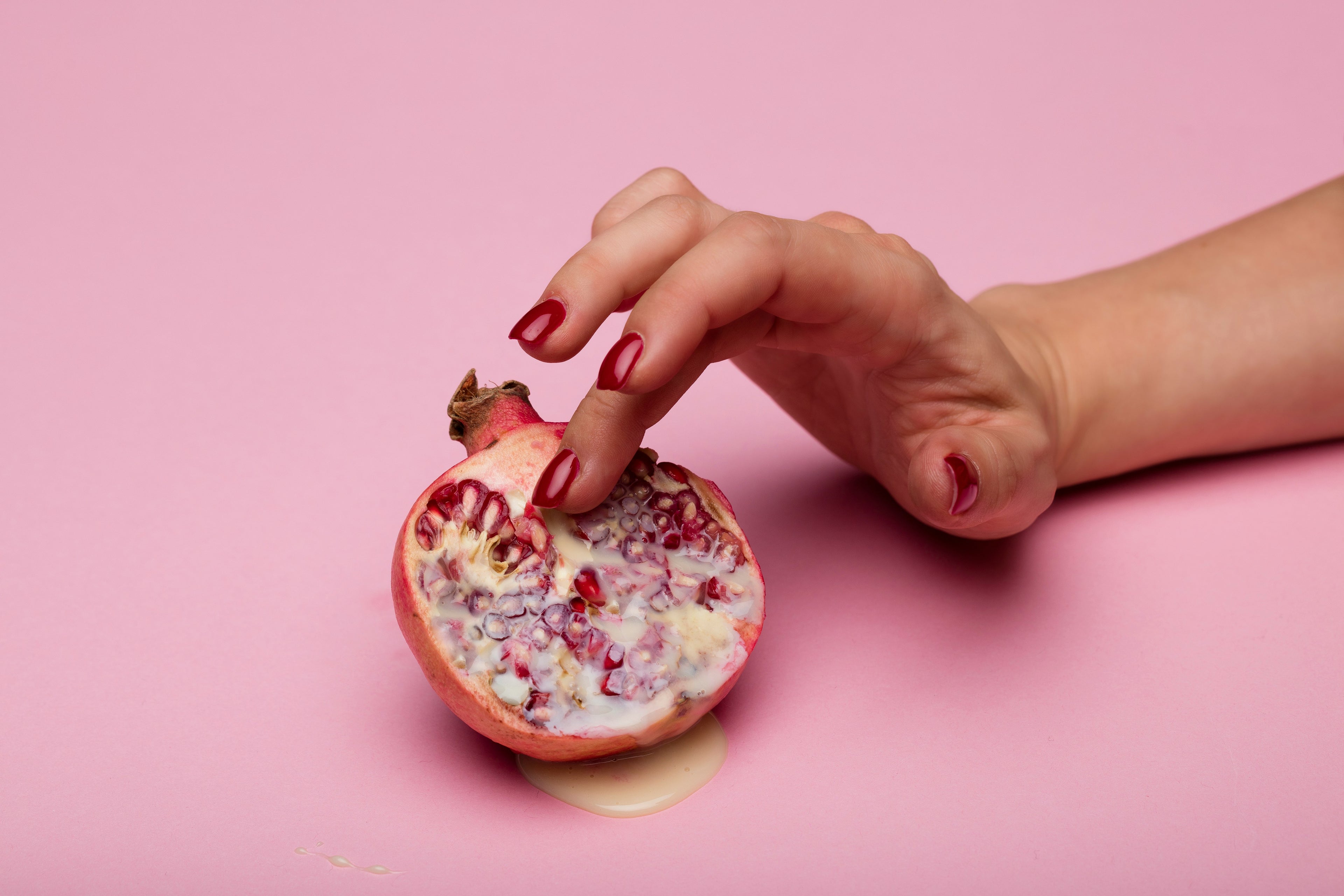 mano femminile con smalto rosso che posa il medio delicatammente nel centro della metà di un melograno
